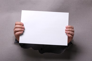 Photo of Man holding sheet of paper through hole in white paper, closeup. Mockup for design