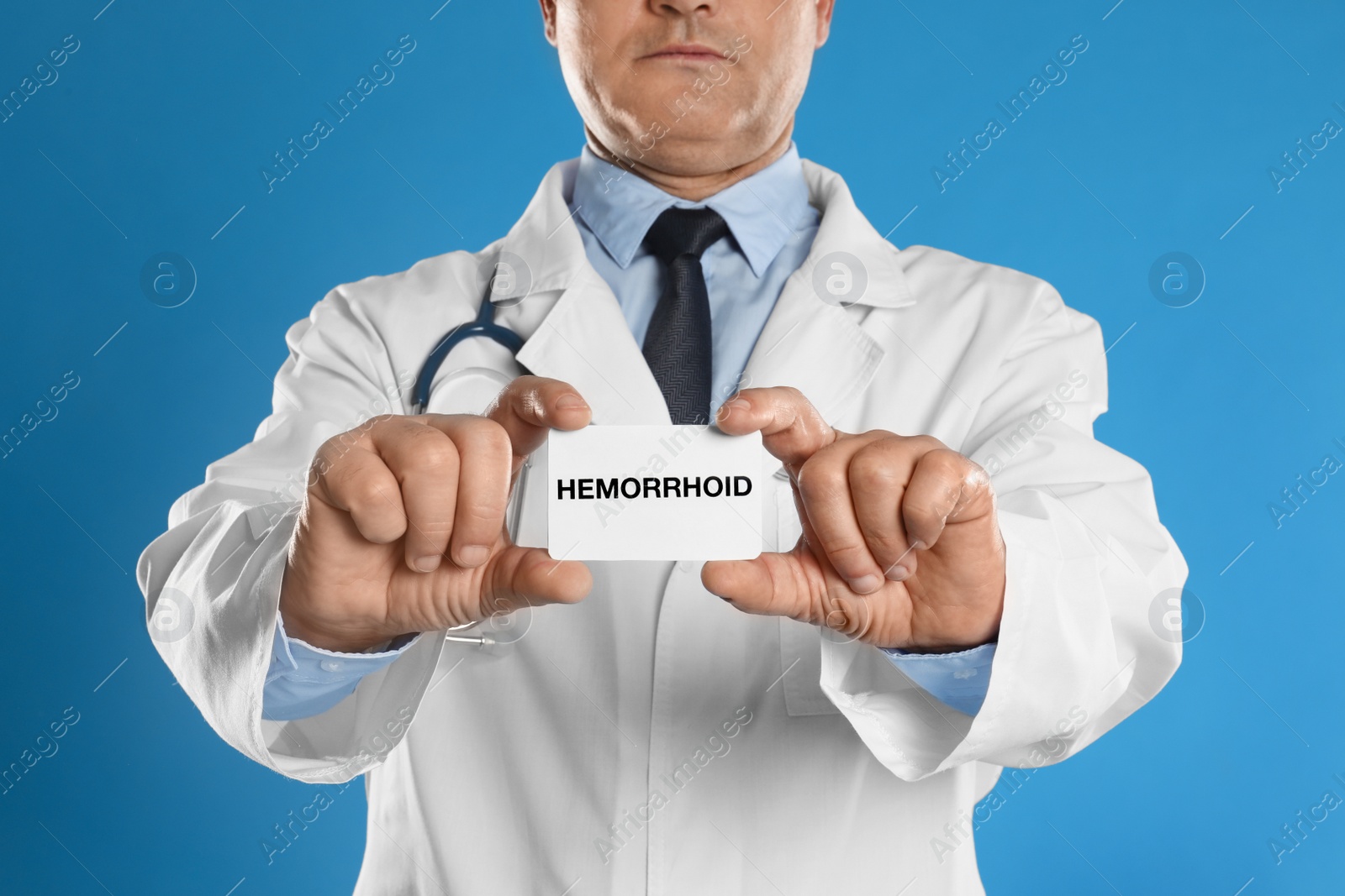 Photo of Doctor holding business card with word HEMORRHOID on blue background, closeup