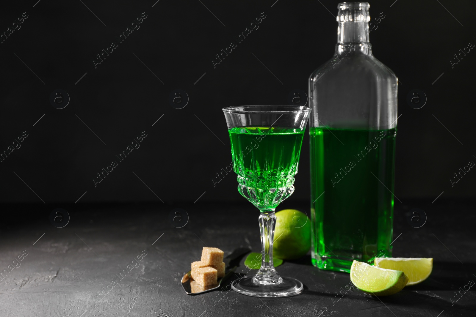 Photo of Absinthe, spoon, brown sugar and lime on black table, space for text. Alcoholic drink