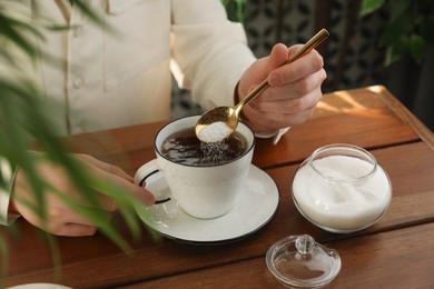 Woman adding sugar into aromatic tea at wooden table indoors, closeup