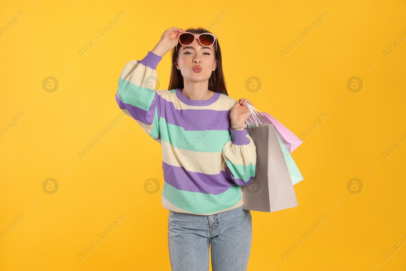 Photo of Beautiful young woman with shopping bags on yellow background. Big sale