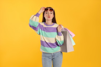 Photo of Beautiful young woman with shopping bags on yellow background. Big sale