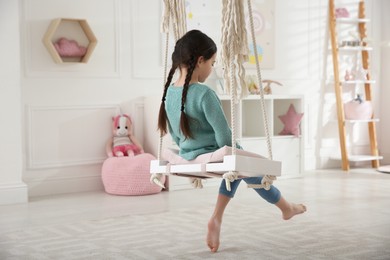 Cute little girl playing on swing at home