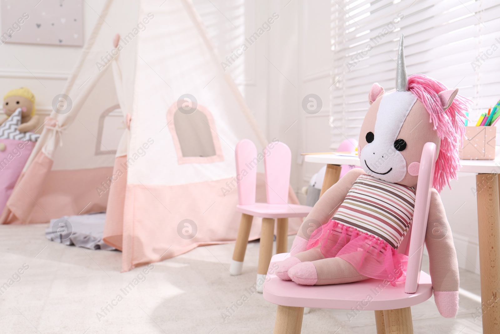 Photo of Cute toy unicorn on chair in stylish playroom, space for text