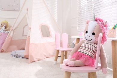 Cute toy unicorn on chair in stylish playroom, space for text