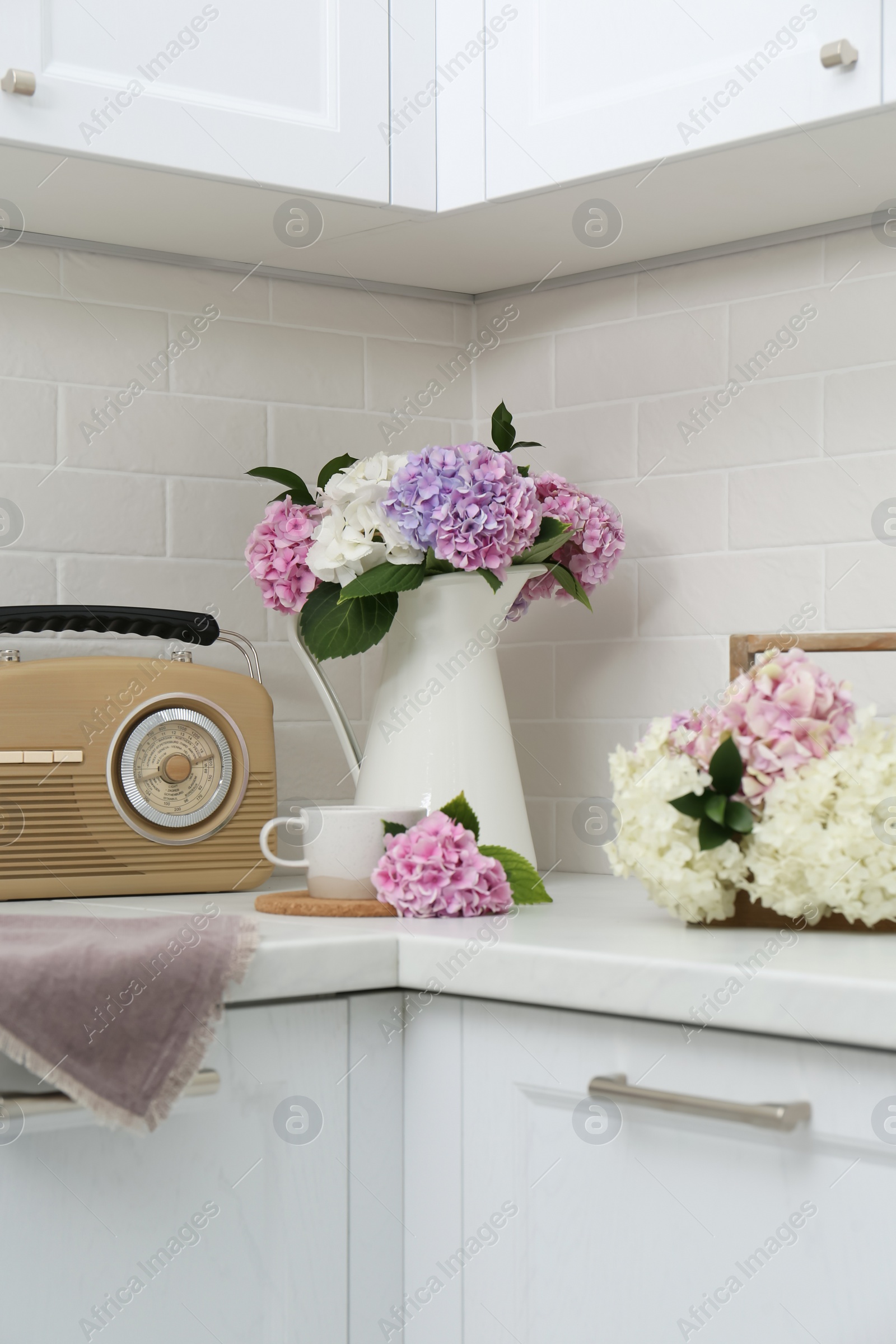 Photo of Beautiful hydrangea flowers, cup and radio set on light countertop