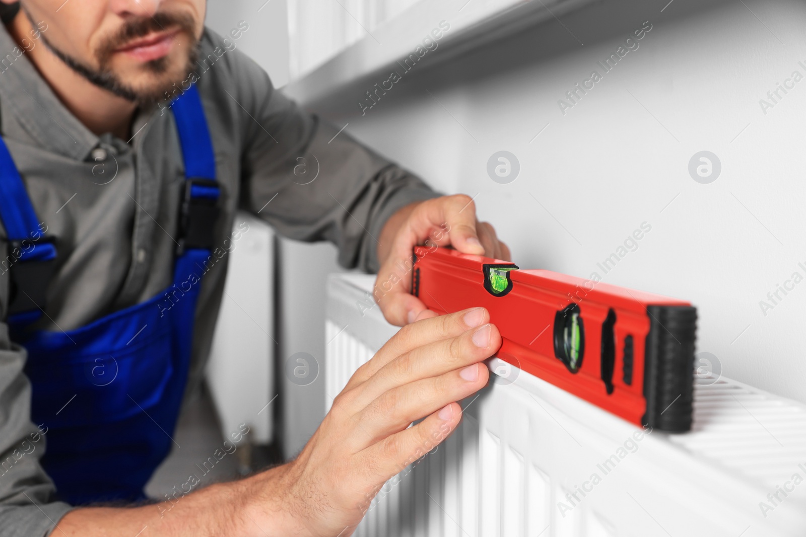 Photo of Professional plumber using bubble level for installing new heating radiator indoors, closeup