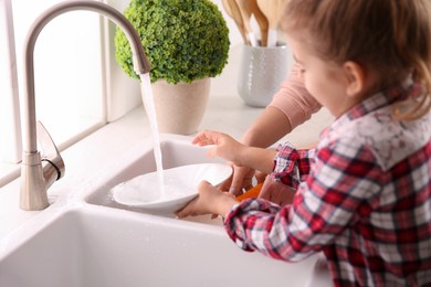 Mother and daughter washing dishes together in kitchen at home, closeup