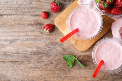 Photo of Tasty strawberry milk shake in plastic cups on wooden table, flat lay. Space for text