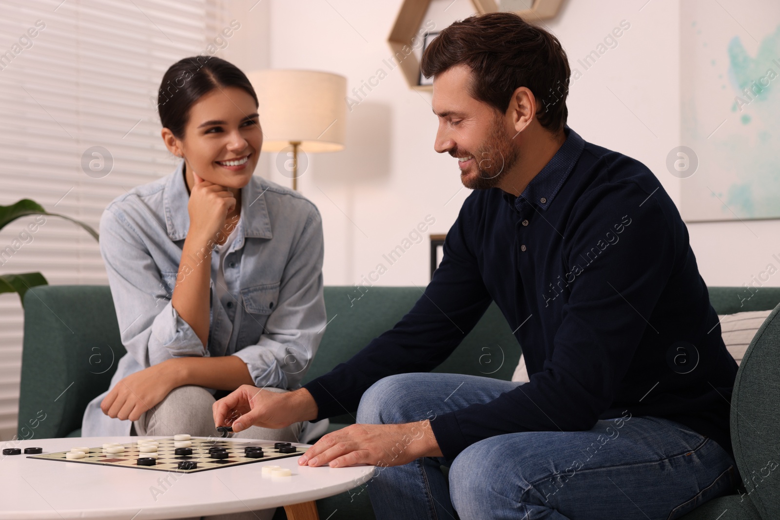 Photo of Couple playing checkers at coffee table at home