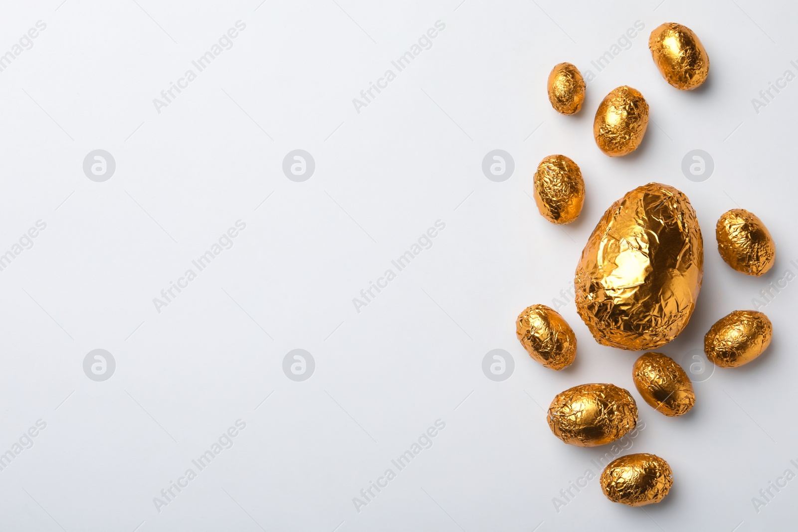 Photo of Chocolate eggs wrapped in golden foil on white background, flat lay. Space for text
