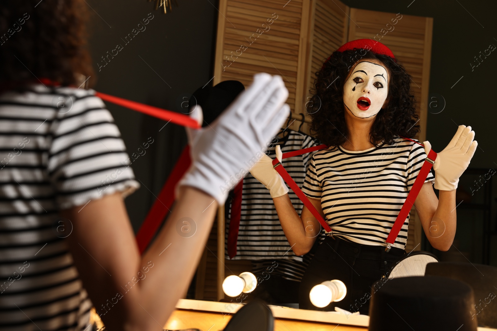 Photo of Young woman in mime costume posing near mirror indoors