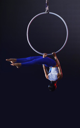 Photo of Young woman performing acrobatic element on aerial ring against dark background