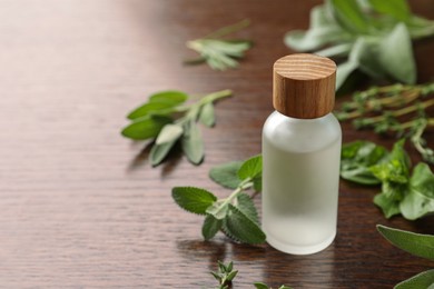 Photo of Bottle of essential oil and fresh herbs on wooden table. Space for text