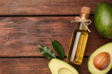 Glass bottle of cooking oil and fresh avocados on wooden table, flat lay. Space for text
