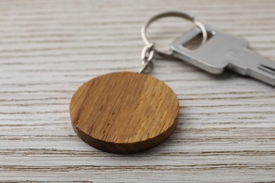 Photo of Key with keychain in shape of smiley face on light wooden background, closeup