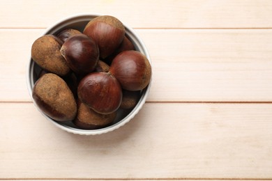 Photo of Sweet fresh edible chestnuts on light wooden table, top view. Space for text