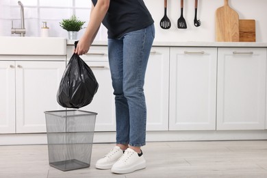 Photo of Woman taking garbage bag out of trash bin in kitchen, closeup