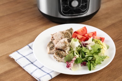 Photo of Delicious chicken with vegetables and modern multi cooker on wooden table