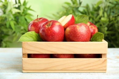 Photo of Wooden crate with ripe juicy red apples on white table against blurred background