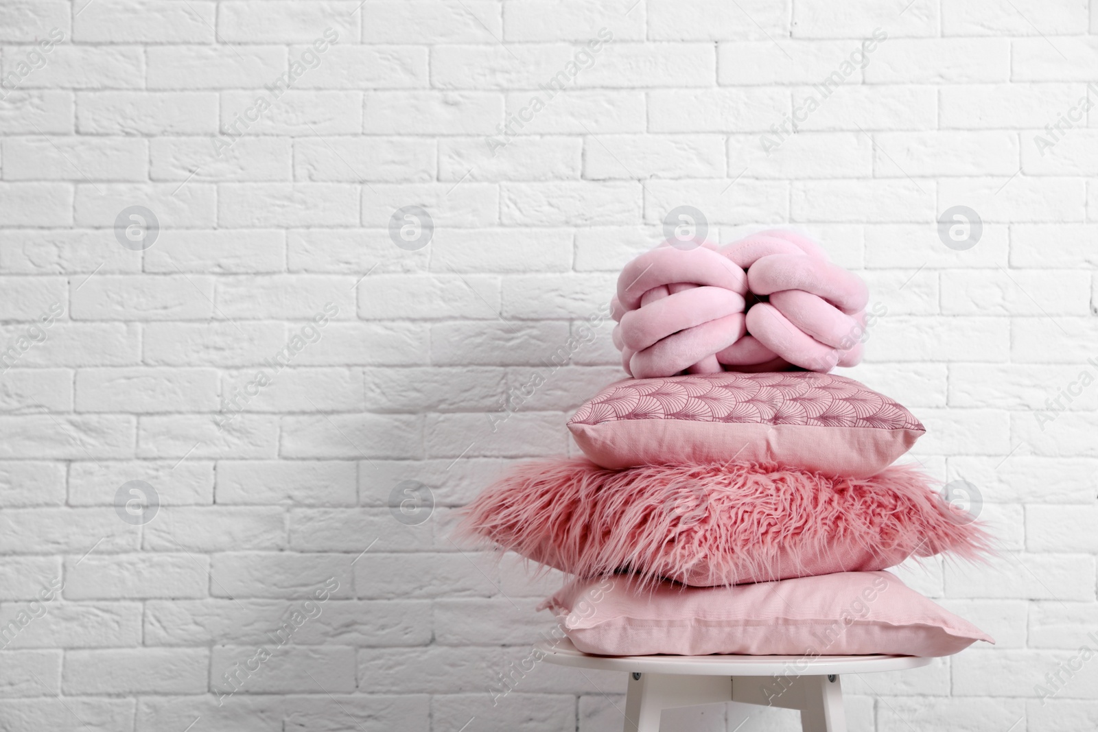 Photo of Many different pillows on chair near brick wall with space for text