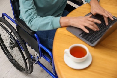 Photo of Woman in wheelchair using laptop at wooden table, selective focus