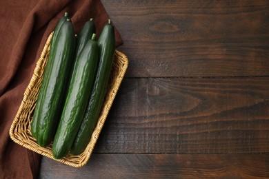 Photo of Fresh cucumbers in wicker basket on wooden table, top view. Space for text