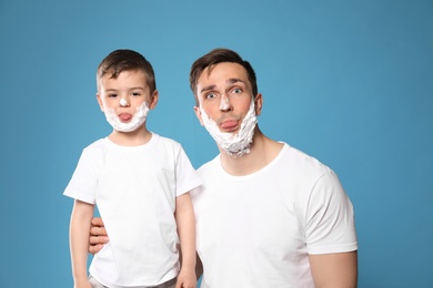 Funny dad and his little son with shaving foam on faces against color background