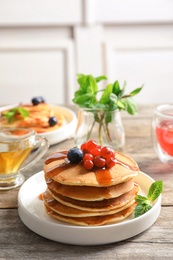 Stack of tasty pancakes with berries and syrup on table