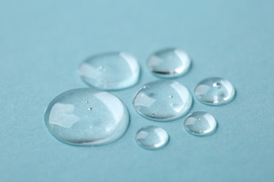 Photo of Drops of cosmetic serum on light blue background, closeup