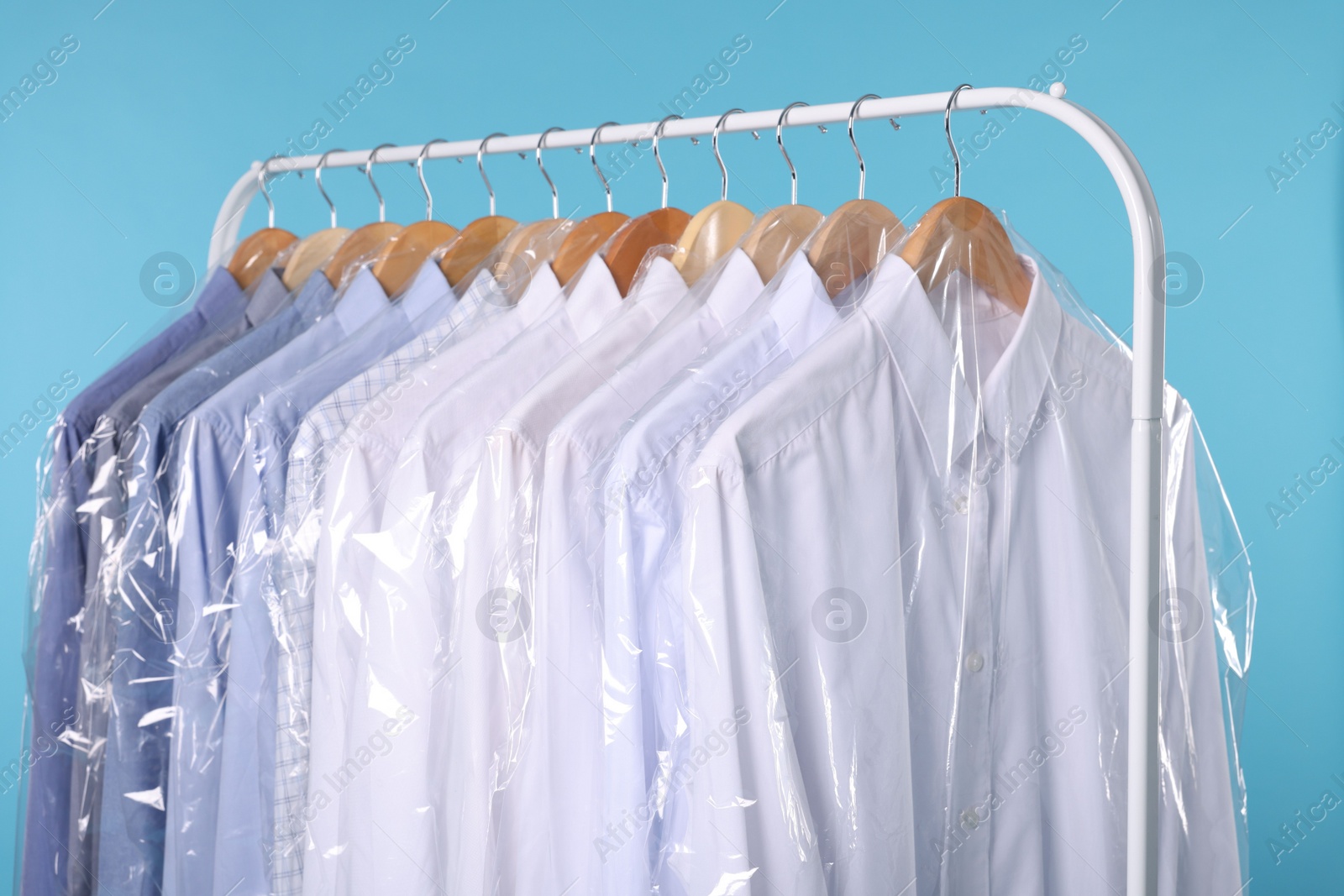 Photo of Dry-cleaning service. Many different clothes in plastic bags hanging on rack against light blue background