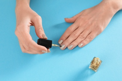 Woman applying nail polish on color background, closeup