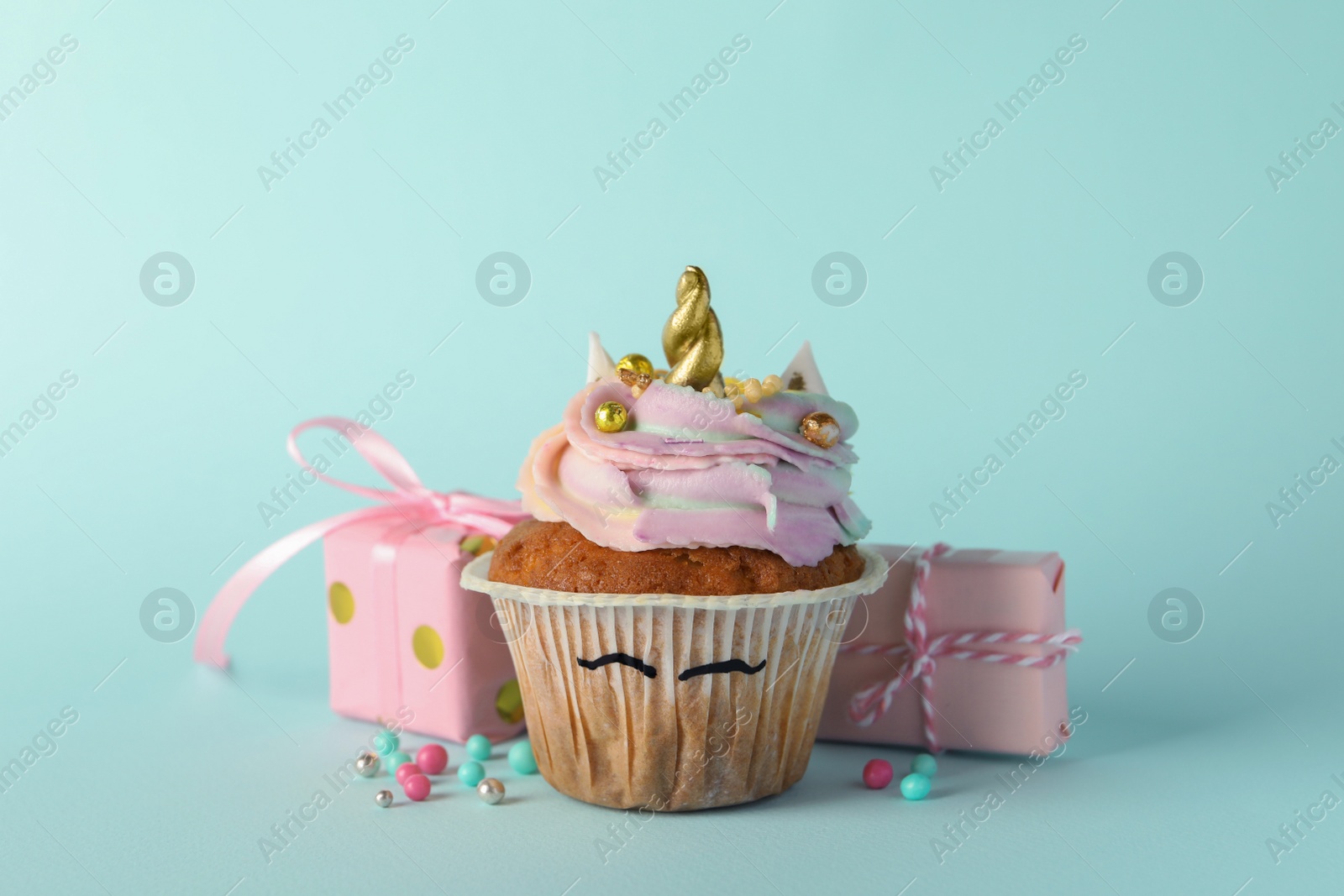 Photo of Cute sweet unicorn cupcake and gift boxes on light turquoise background