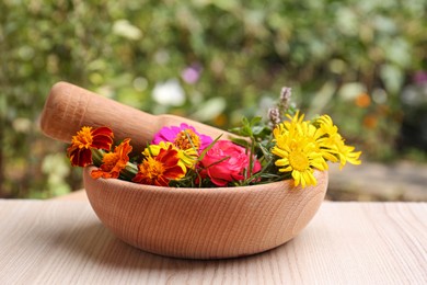 Mortar with pestle and beautiful fresh flowers on wooden table outdoors