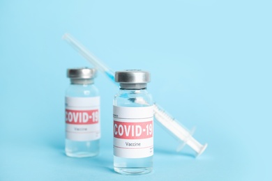 Photo of Vials with coronavirus vaccine and syringe on light blue background