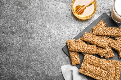 Photo of Delicious sweet kozinaki bars, honey and milk on grey table, flat lay. Space for text