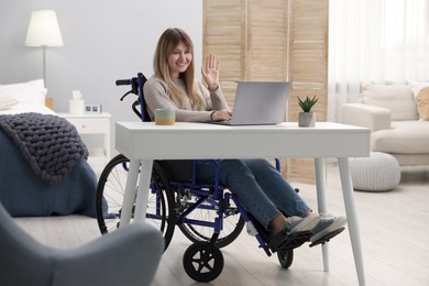 Photo of Woman in wheelchair having video chat via laptop at table in home office