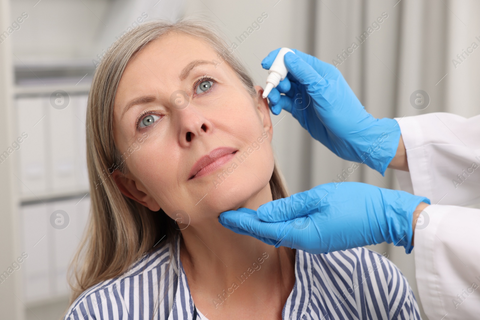 Photo of Medical drops. Doctor dripping medication into woman's ear indoors