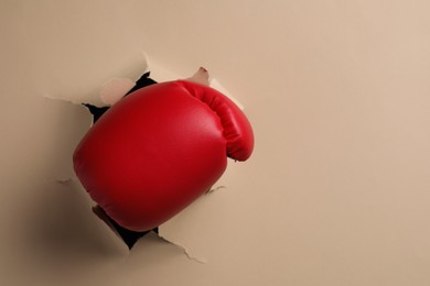 Photo of Man breaking through beige paper with boxing glove, closeup. Space for text