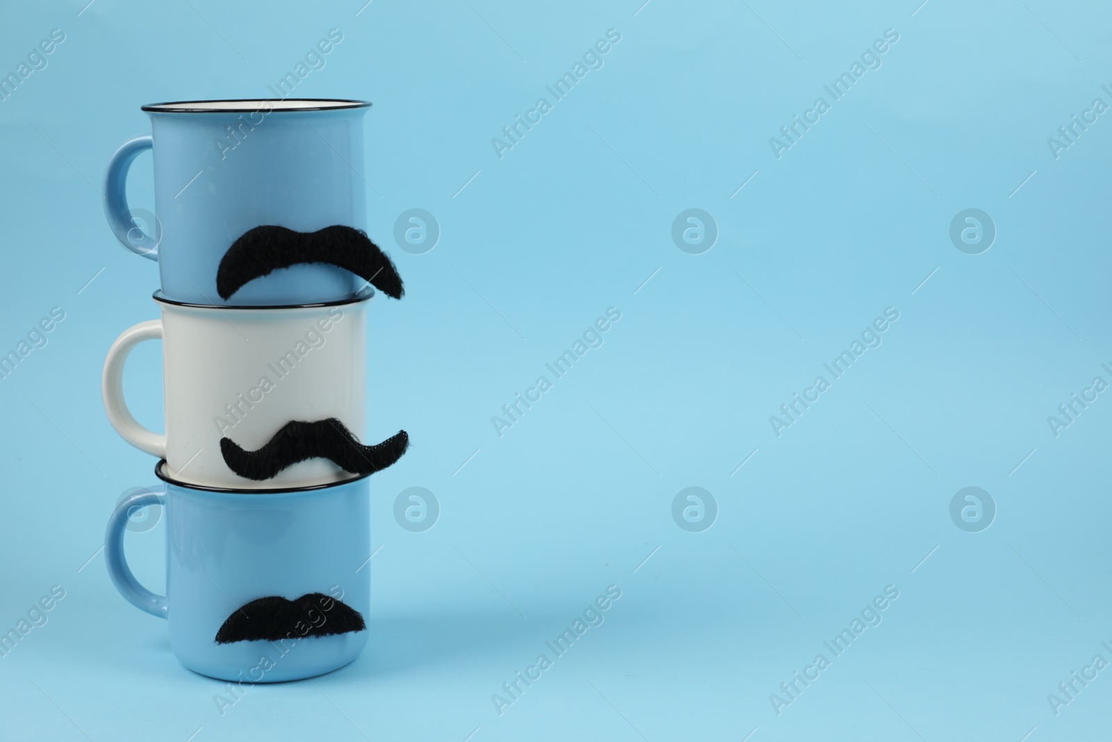 Photo of Cups with fake mustaches on light blue background. Space for text