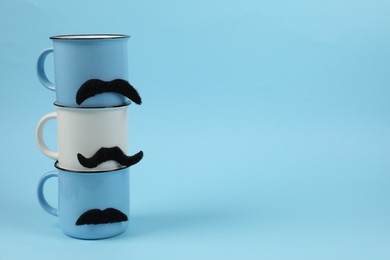 Photo of Cups with fake mustaches on light blue background. Space for text