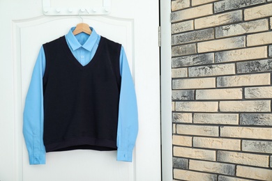 School uniform for boy hanging on white door