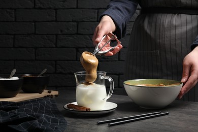 Woman making dalgona coffee at grey table, closeup