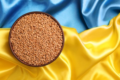 Photo of Bowl of wheat grains on Ukrainian flag, top view. Space for text
