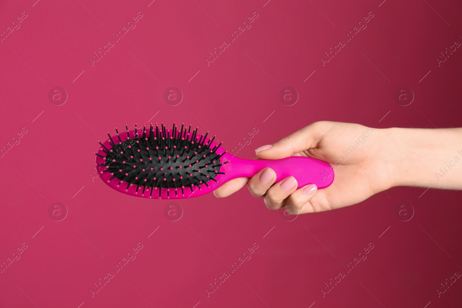 Photo of Woman holding hair brush against crimson background, closeup