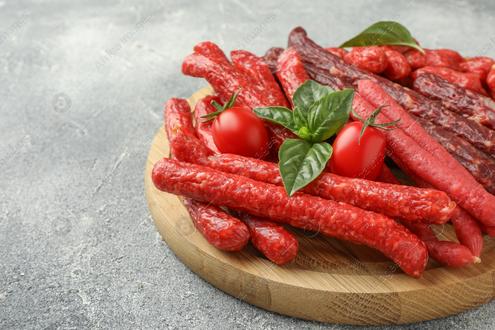 Photo of Different thin dry smoked sausages, basil and tomatoes on light grey table, closeup. Space for text