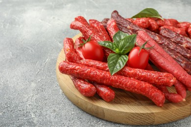 Photo of Different thin dry smoked sausages, basil and tomatoes on light grey table, closeup. Space for text