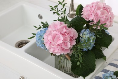 Photo of Vase with beautiful hortensia flowers in kitchen sink