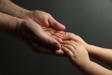 Photo of Father and child holding hands on dark grey background, closeup