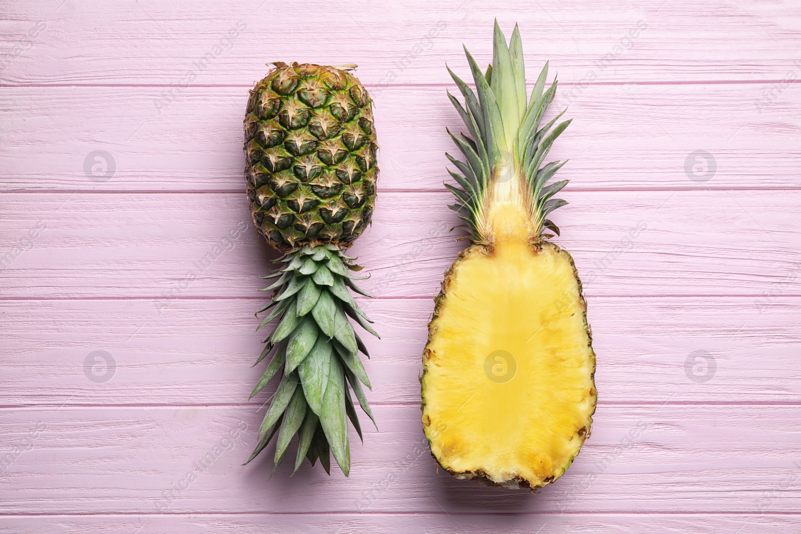 Photo of Fresh whole and cut pineapples on pink wooden background, top view